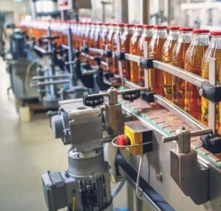 A row of plastic bottles filled with liquid moves along a conveyor belt in a beverage production facility, where sweetener labeling ensures accurate ingredient information for consumers.