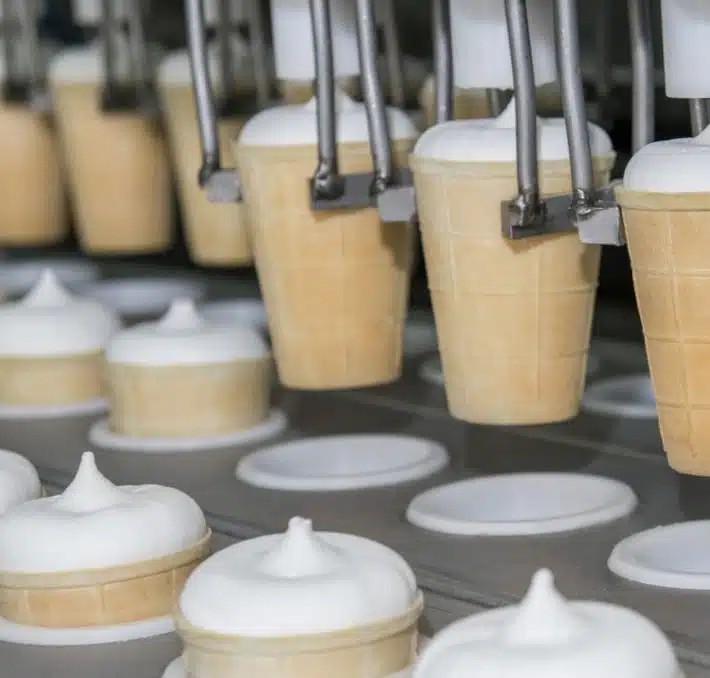 Eistüten, die von einer Maschine in einer Produktionslinie mit Vanille-Softeis gefüllt werden.
