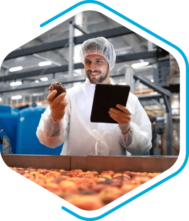 A worker in protective clothing inspects fruit and records data on a tablet, utilizing PLM for food and beverage in a modern processing facility.